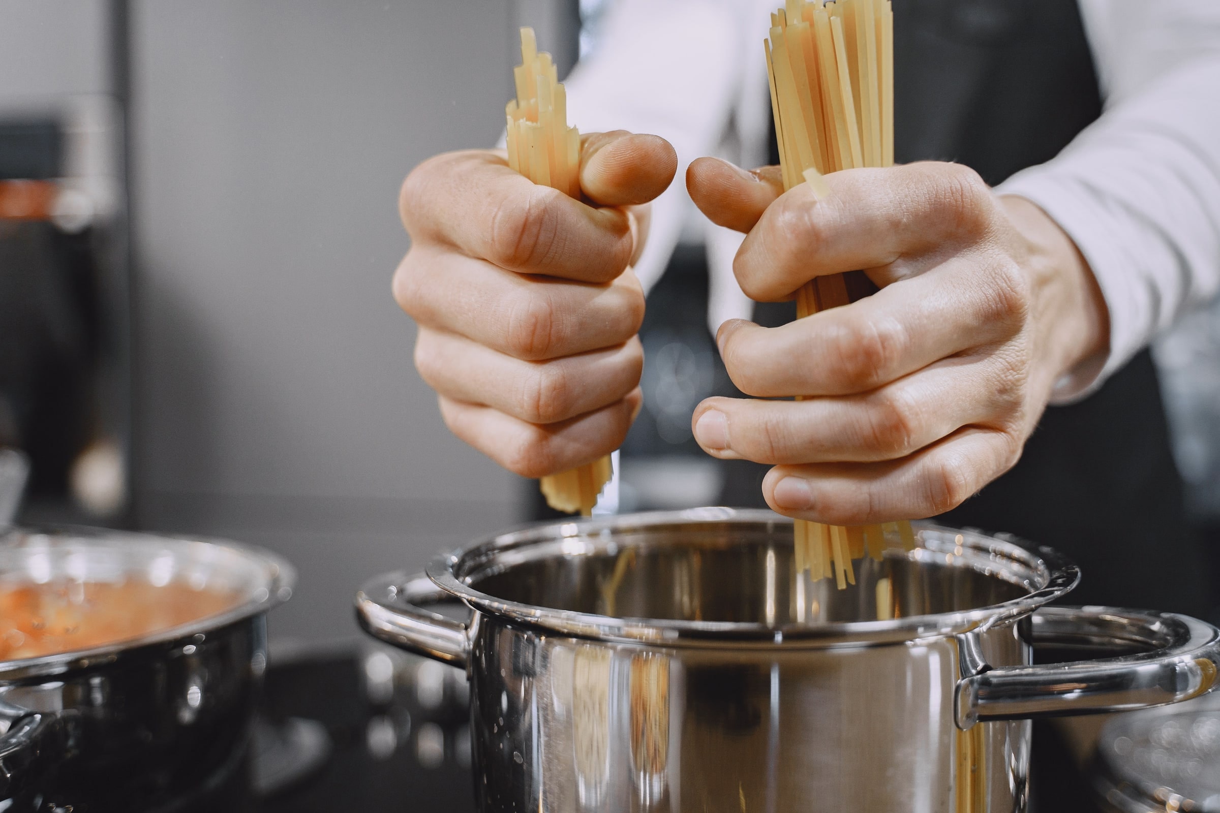Des mains de chef ajoutent des pâtes fraîches dans une casserole
